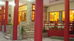 A building with stone walls and red pillars, featuring a staircase leading to a balcony with outdoor seating. - Hotel Arenales (Villa Carlos Paz)