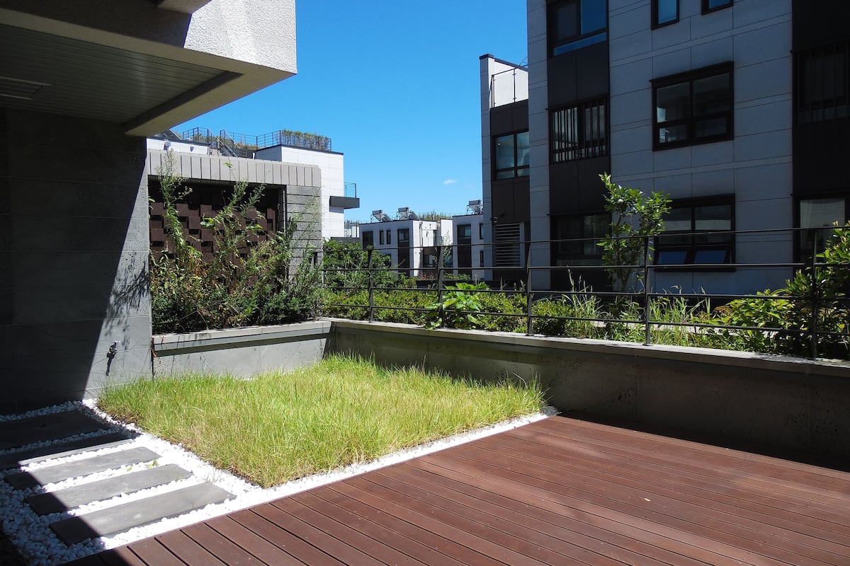 Une terrasse extérieure moderne avec une plateforme en bois, des jardinières en béton agrémentées de plantes et une vue sur les bâtiments voisins.