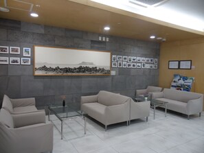 Un área de recepción con sofás color beige, una mesa de centro de vidrio, cuadros enmarcados en la pared y una pared de piedra.