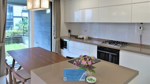 Une cuisine moderne avec des meubles blancs, une table à manger en bois et une vue sur l’extérieur grâce à une porte coulissante.