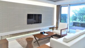 Un salon moderne doté d’un téléviseur à écran plat fixé sur un mur texturé, d’un canapé, d’une table basse et offrant une vue sur l’extérieur grâce à de grandes fenêtres.