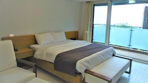 Une chambre d’hôtel moderne avec un grand lit, une table de chevet, une chaise et une vue sur l’eau par la fenêtre.