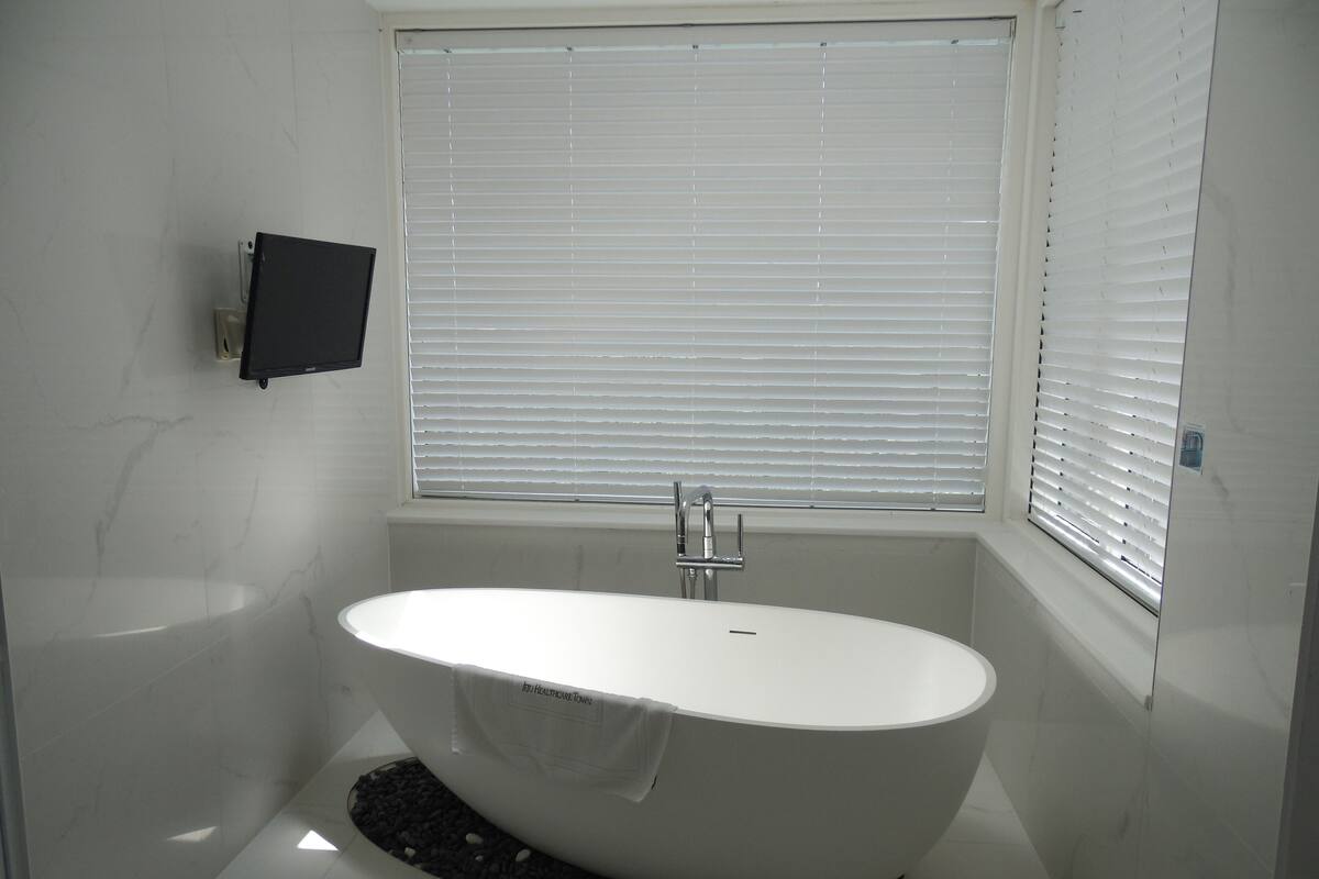 Une salle de bain moderne avec une baignoire sur pieds, des toilettes et une fenêtre équipée de stores.