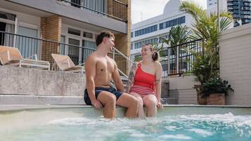 A couple sitting by a pool with a building in the background.