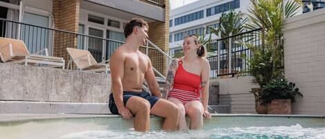 Una pareja sentada junto a una piscina, con un edificio al fondo.