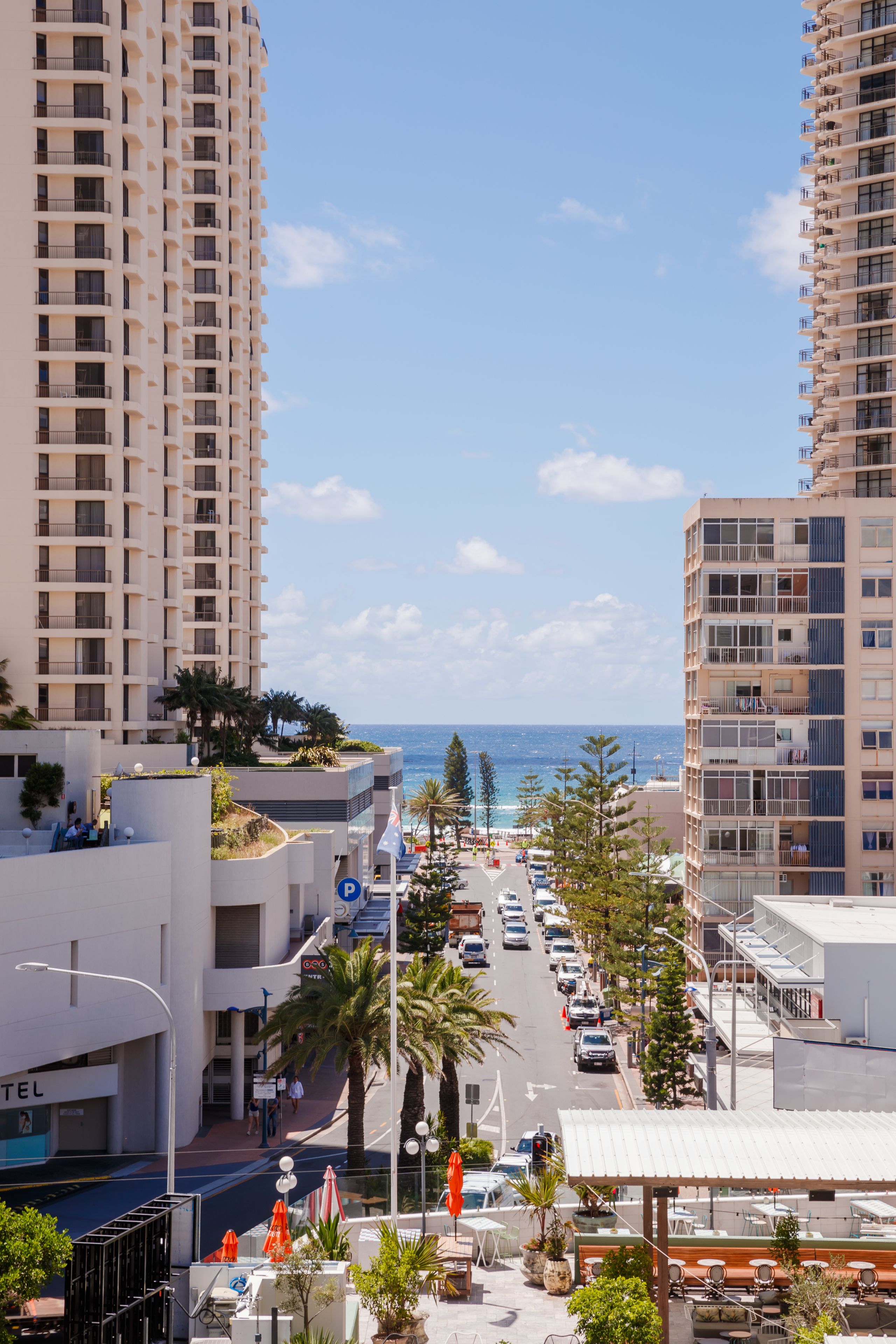 Un carrer urbà a la costa, amb edificis alts, cel clar i vista al mar.