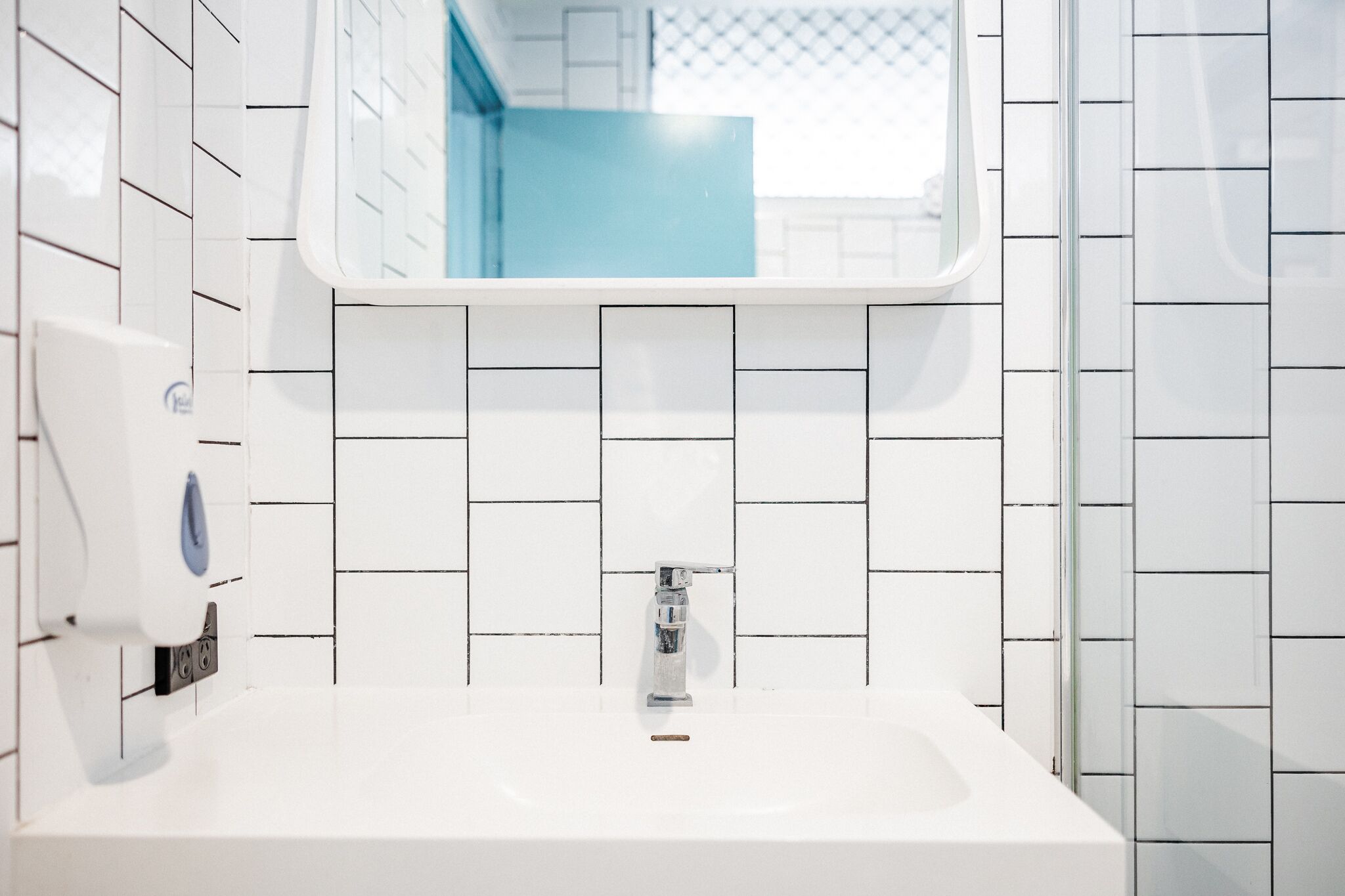 A bathroom with white tiled walls, a white sink, and a mirror above the sink.
