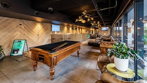 Una mesa de billar, una zona de bar y un área de estar con un ventanal grande.