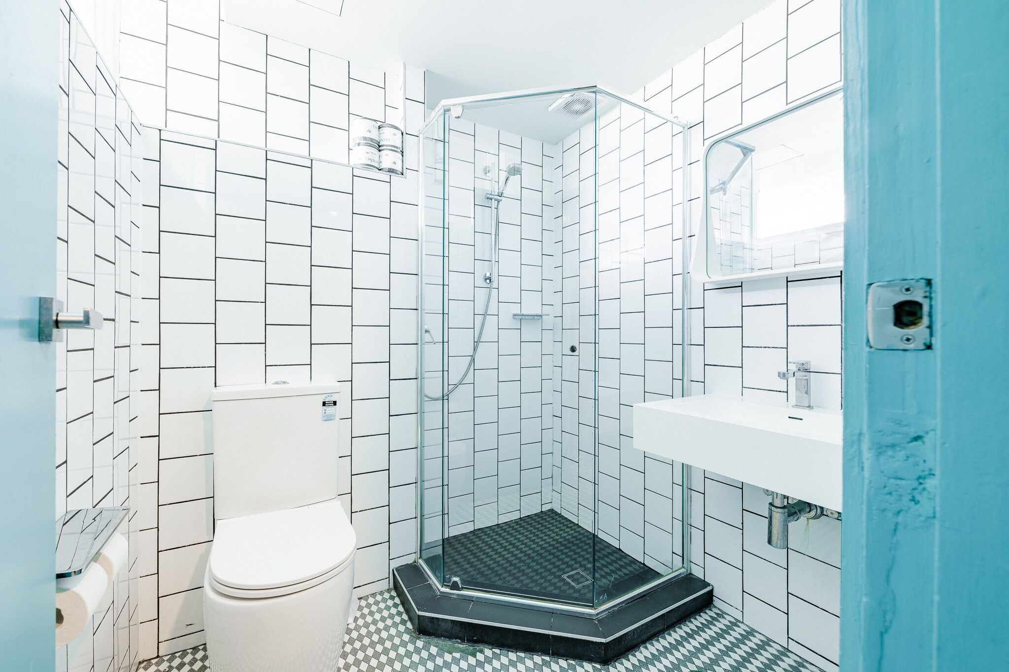 Une salle de bain avec des murs recouverts de carreaux blancs, une douche en verre, des toilettes blanches et un lavabo devant un mur bleu.