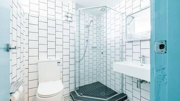 Une salle de bain avec des murs recouverts de carreaux blancs, une douche en verre, des toilettes blanches et un lavabo devant un mur bleu.