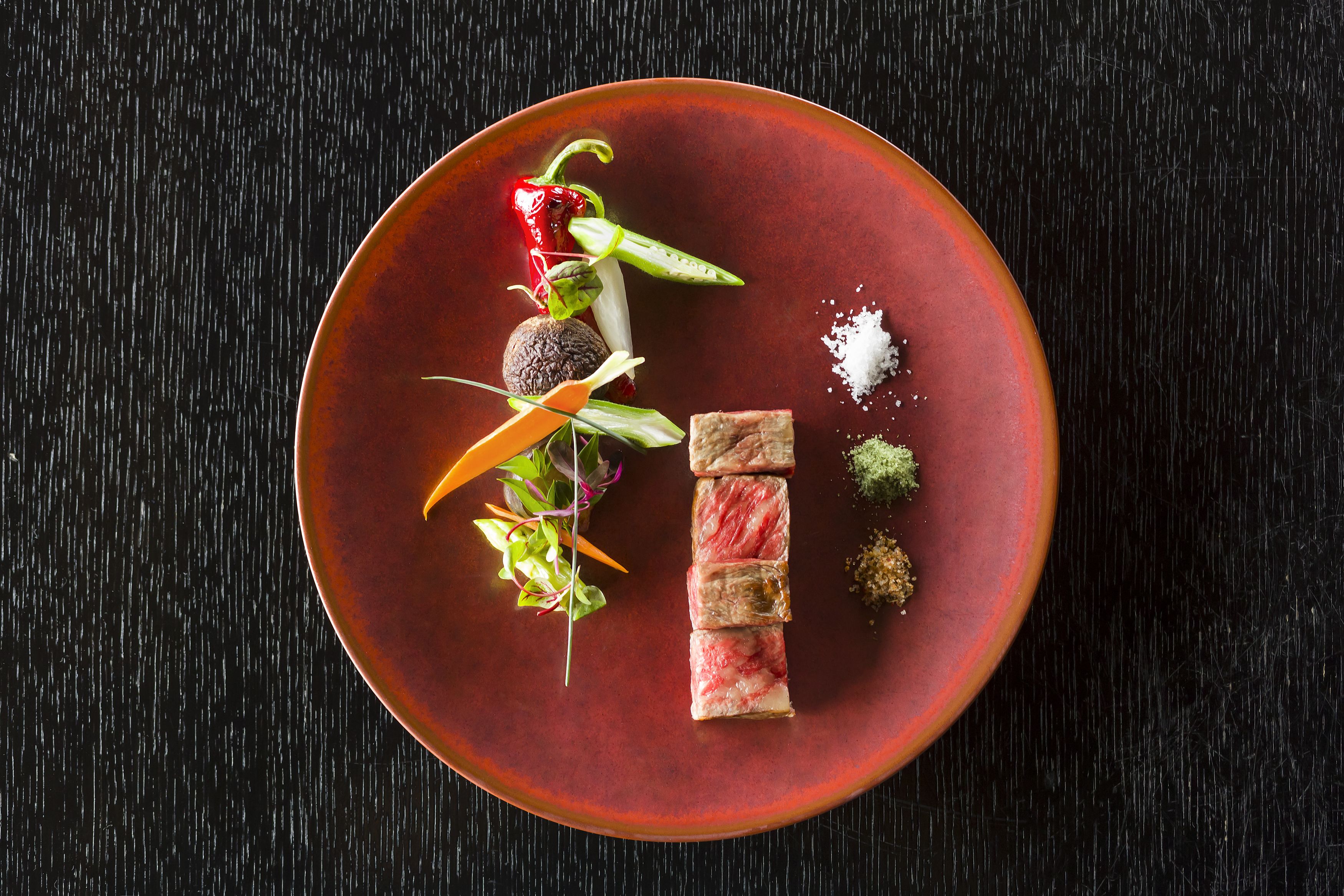 Un plato con distintos alimentos, incluyendo un pimiento rojo, verduras verdes y un trozo de carne.