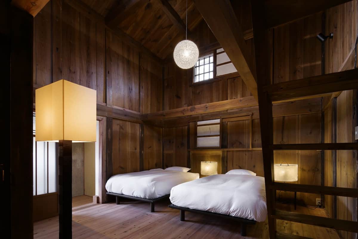 Una habitación rústica de madera con dos camas, una lámpara colgante y una ventana.