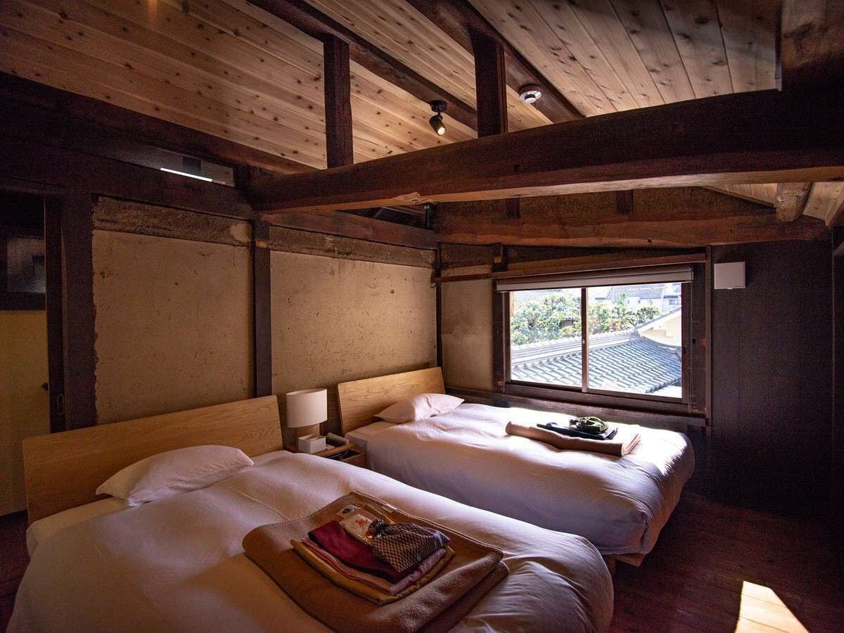 Una habitación con dos camas, vigas de madera, un ventanal con vistas y una mesita de noche con lámpara.