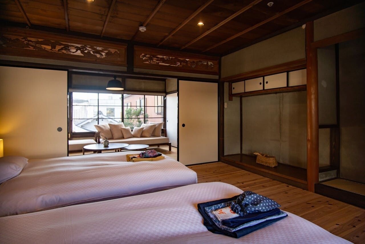A hotel room with two beds, a sofa, a window with a view, and traditional wooden architecture.