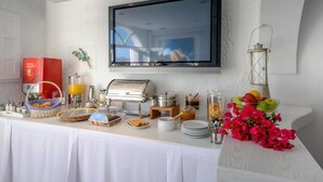 Un buffet de petit-déjeuner avec une télévision au-dessus, une machine à café et divers aliments.