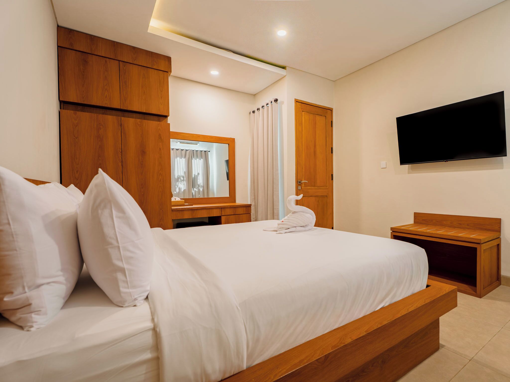 A hotel room with a large bed, wooden headboard, a flat-screen TV mounted on the wall, and a wooden wardrobe.