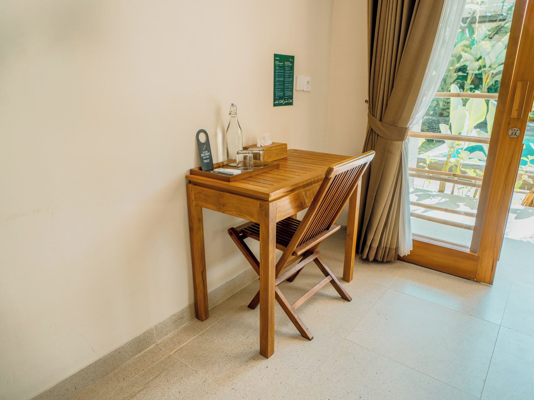 A wooden table with a chair, a bottle, and a tray with glasses and a tissue box.