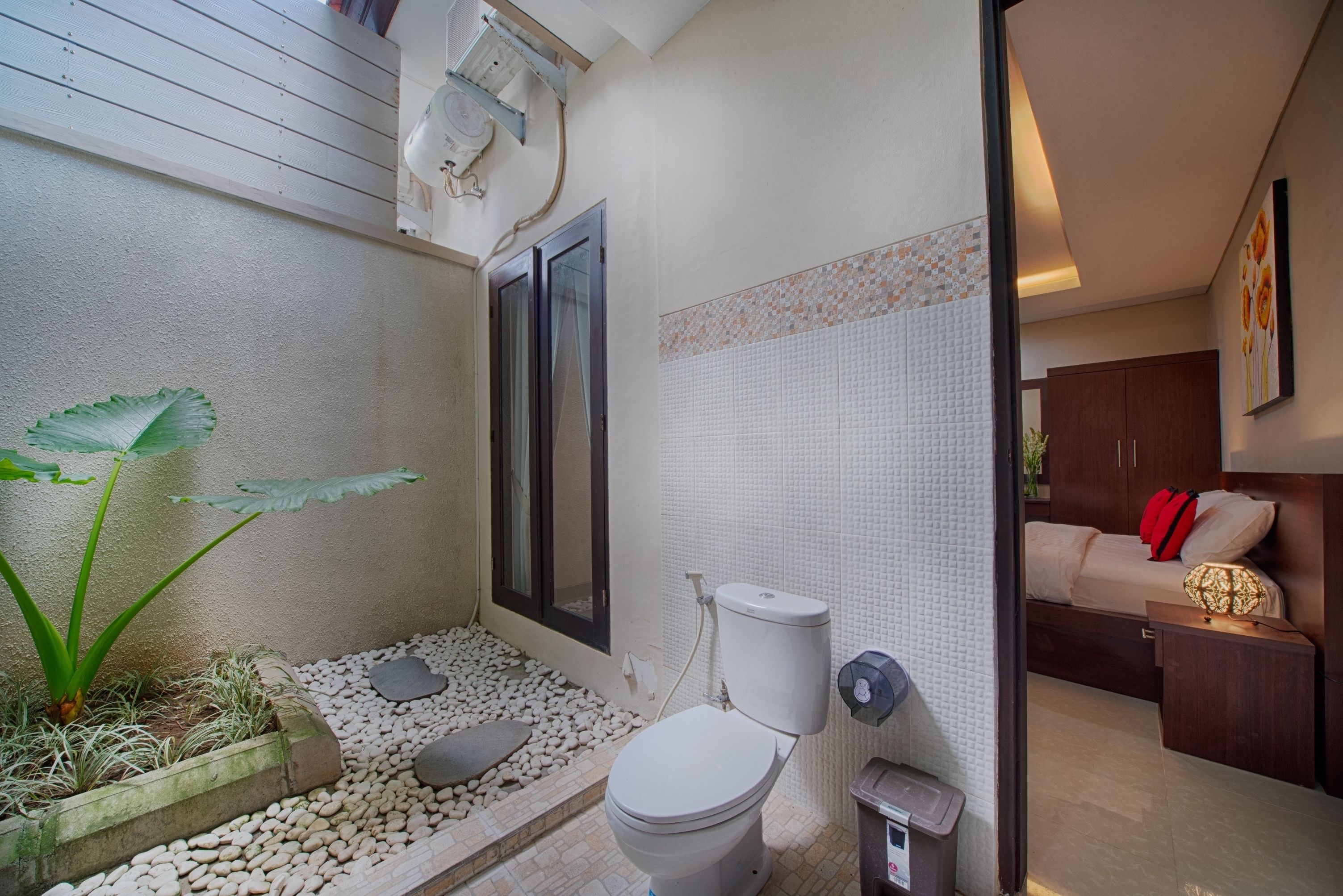 A compact bathroom with a toilet, a shower area, and a small garden bed with plants.
