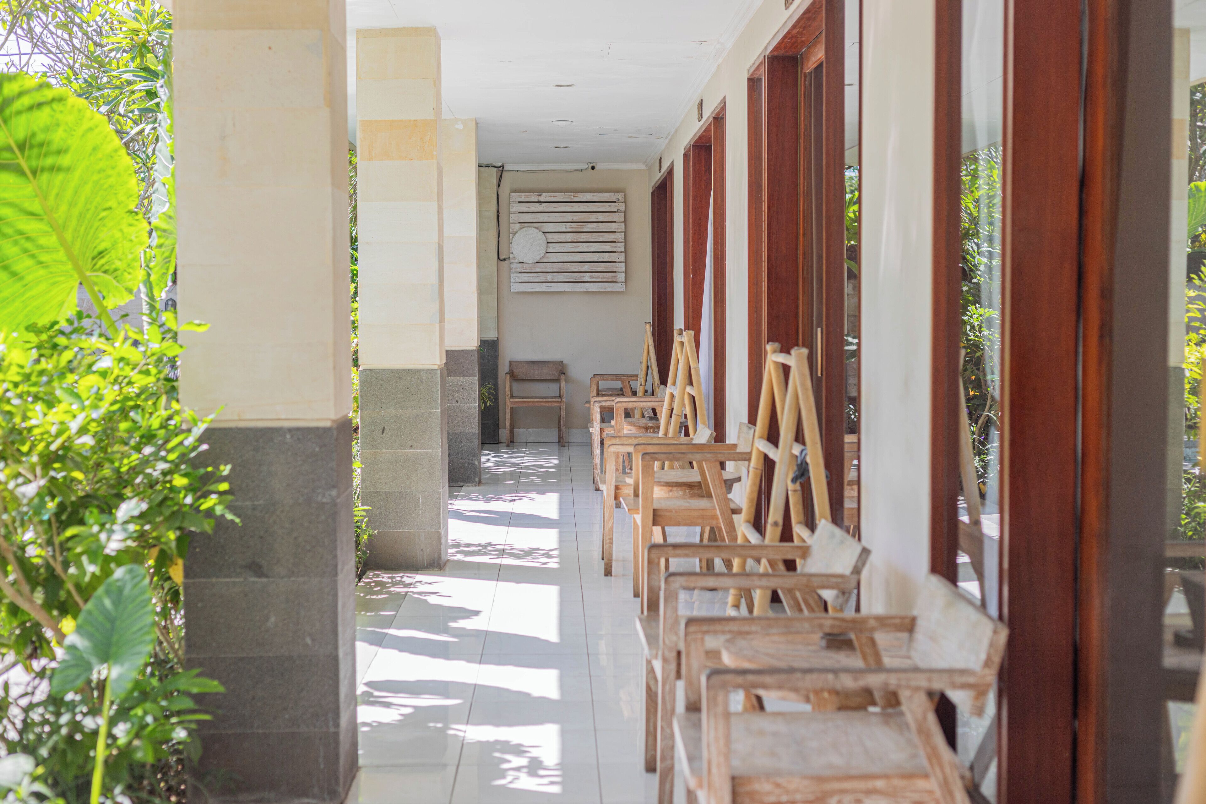 A corridor with wooden chairs aligned against the wall, a bench, and a wooden door frame.