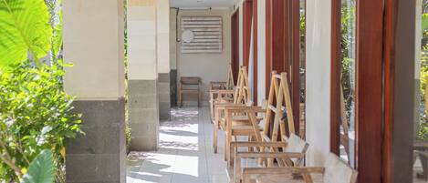 A corridor with wooden chairs aligned against the wall, a bench, and a wooden door frame.