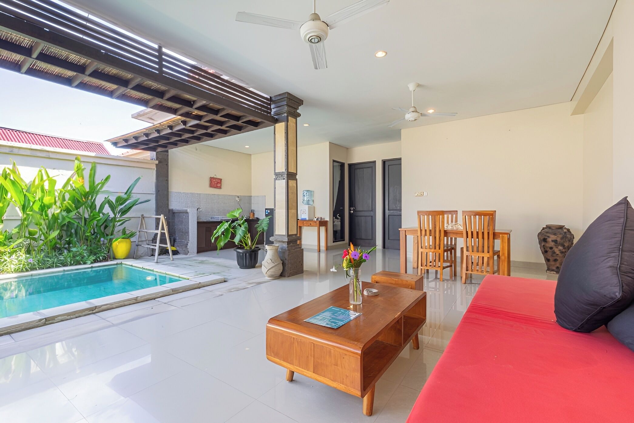 Ein stilvoller Wohnbereich mit Pool, einem roten Sofa, Holzmöbeln und einem Deckenventilator.