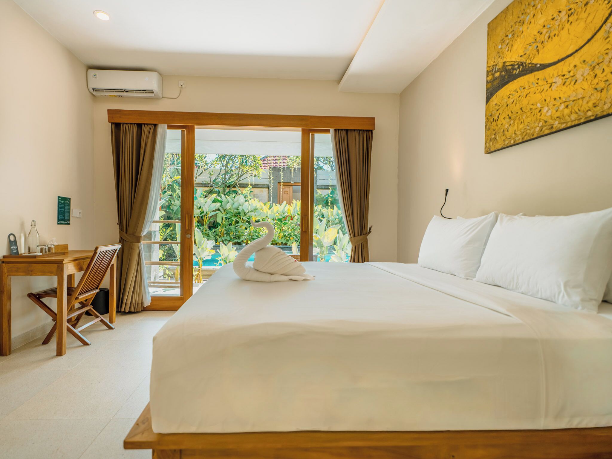 A hotel room with a large bed, a desk with a chair, and a view of the garden through the glass door.