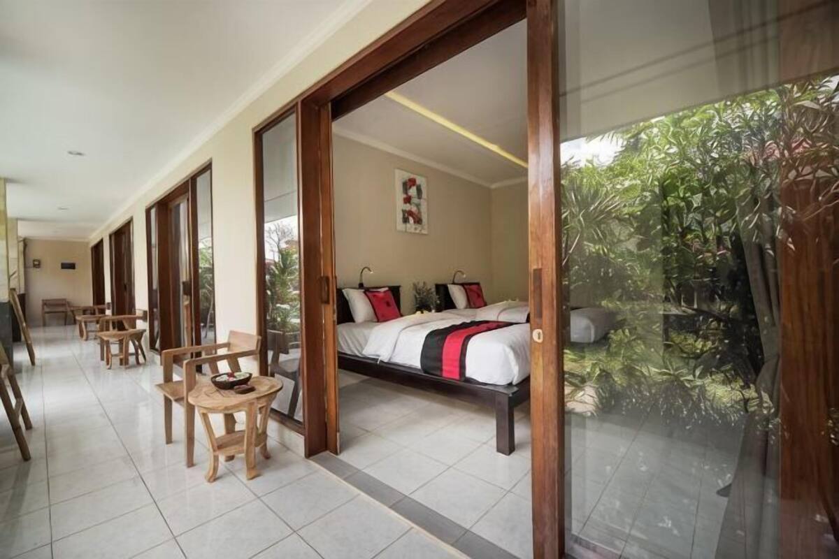 Ein Zimmer mit Bett, Schreibtisch und Stühlen, einem großen Fenster und Blick auf Grünflächen.