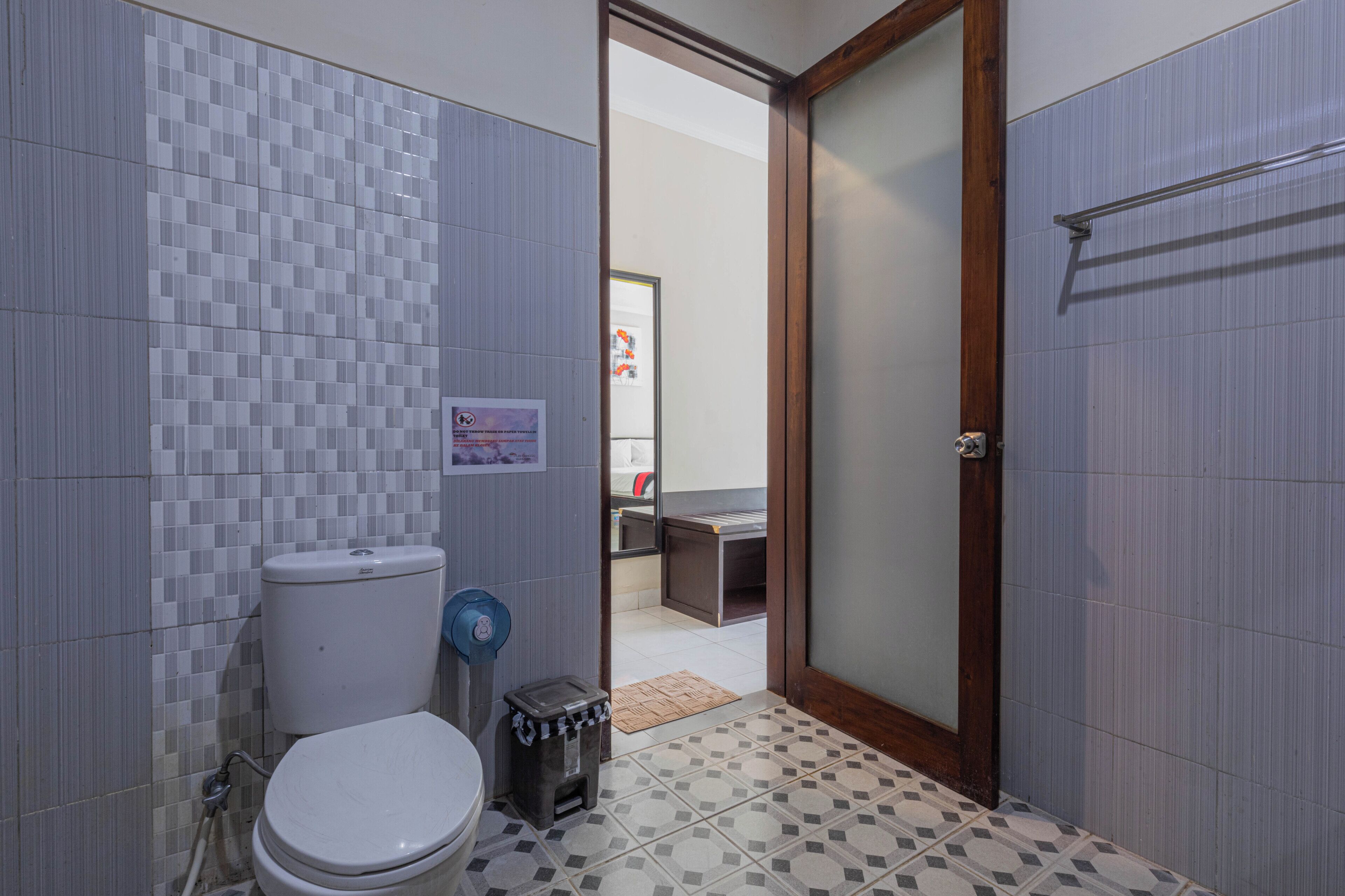 Un baño pequeño con inodoro, un cubo de basura y una zona de ducha visible a través de una puerta abierta.