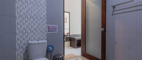 Un baño pequeño con inodoro, un cubo de basura y una zona de ducha visible a través de una puerta abierta.