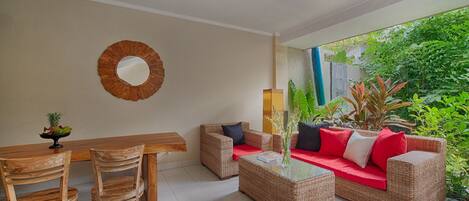 A room with a ceiling fan, a round mirror, wicker furniture, and a view of greenery outside.