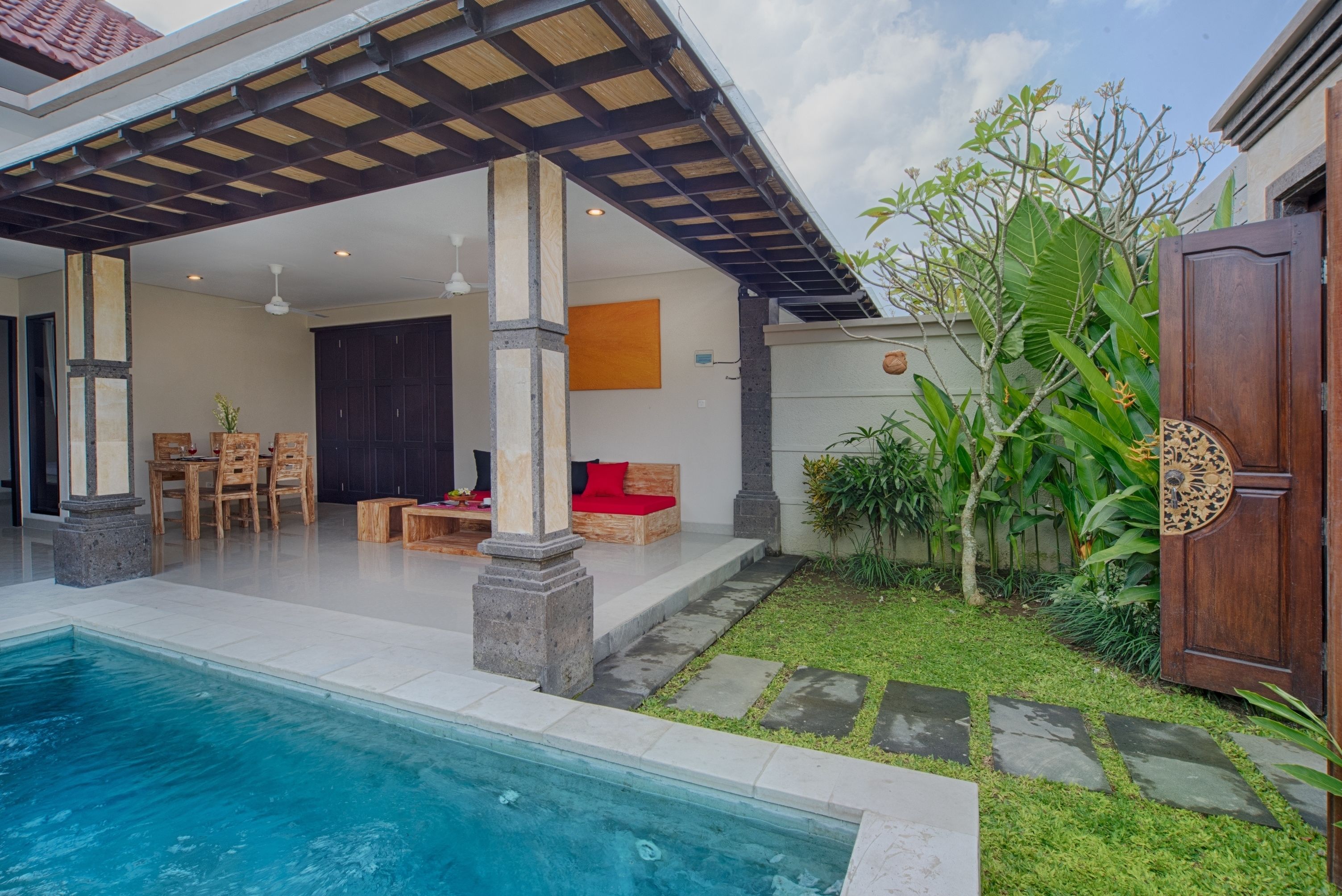 A covered outdoor area with a pool, seating, and a garden.
