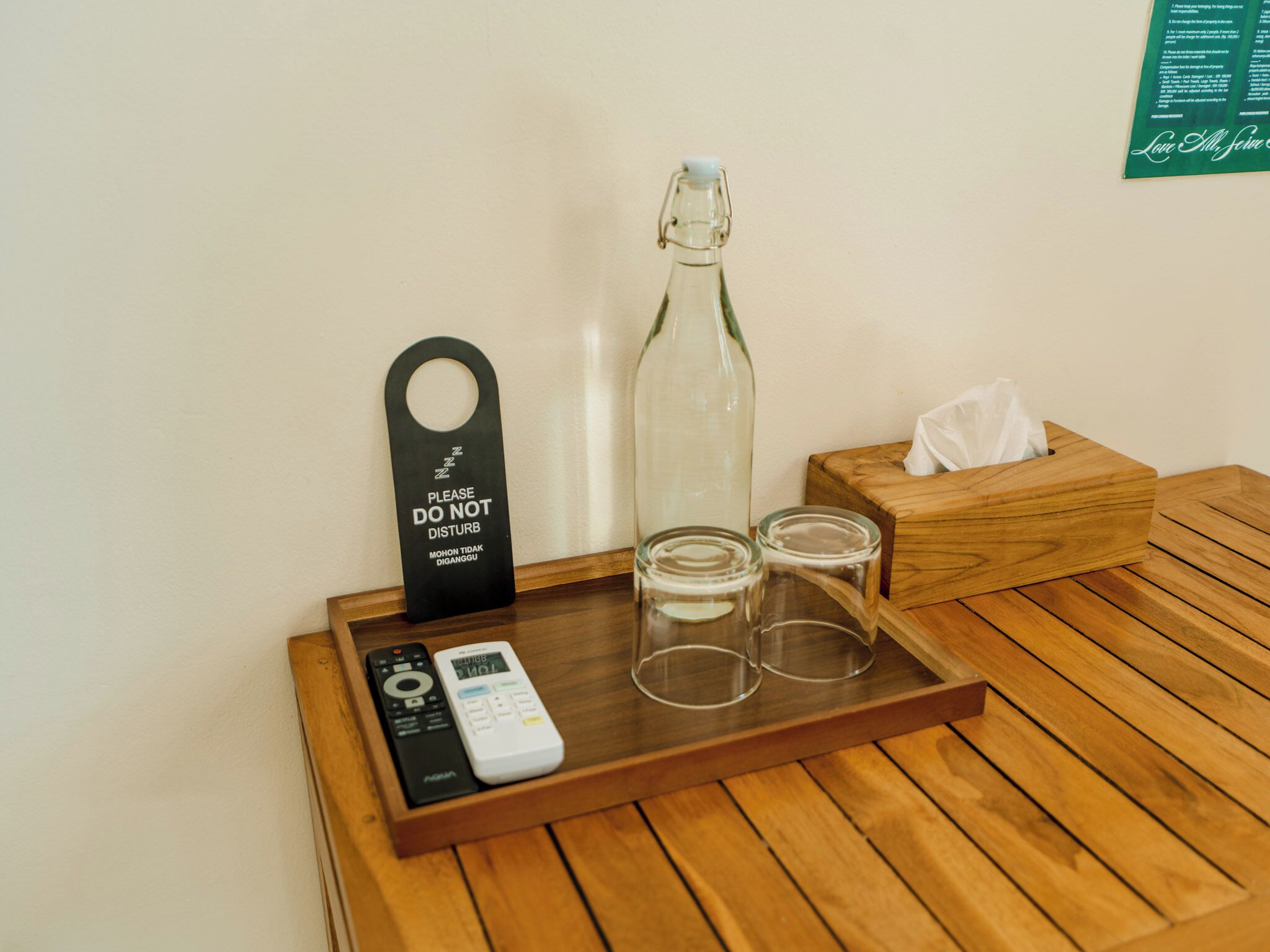 A wooden tray with a remote control, a glass bottle, two glasses, and a 'Please Do Not Disturb' sign.