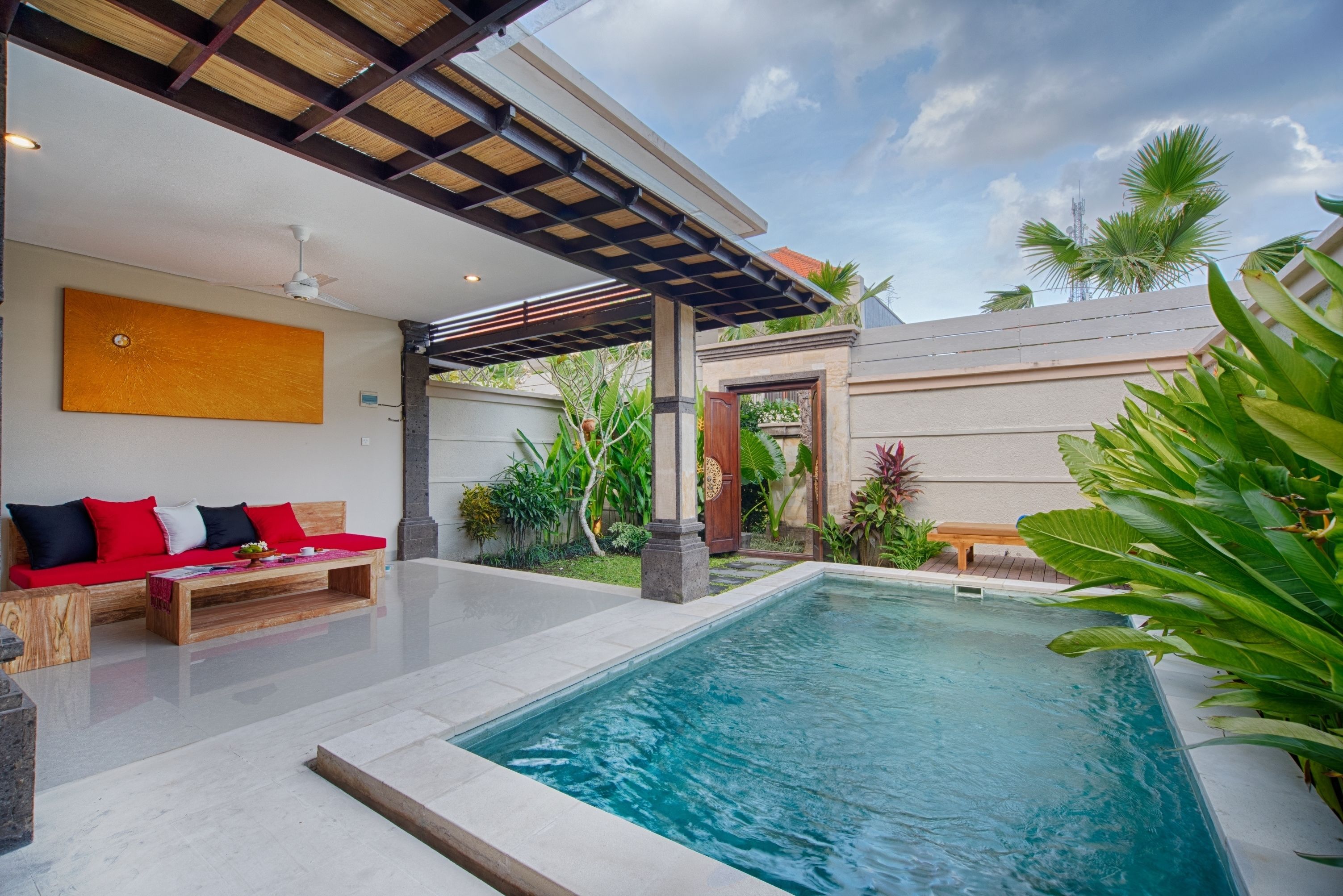 A modern outdoor pool area with a wooden deck, a red sofa, and a pergola.