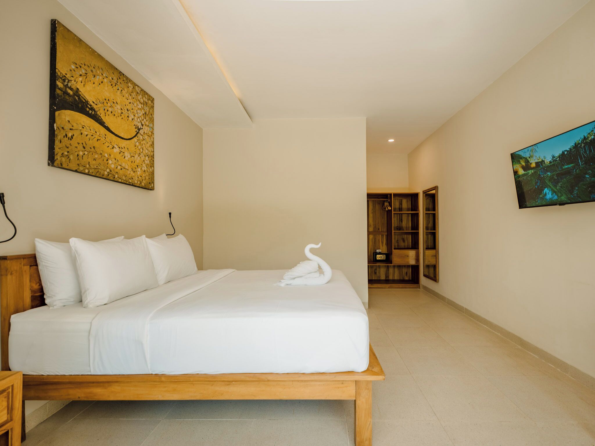 A hotel room with a large bed, a wooden headboard, a painting on the wall, a television, and a wooden wardrobe.