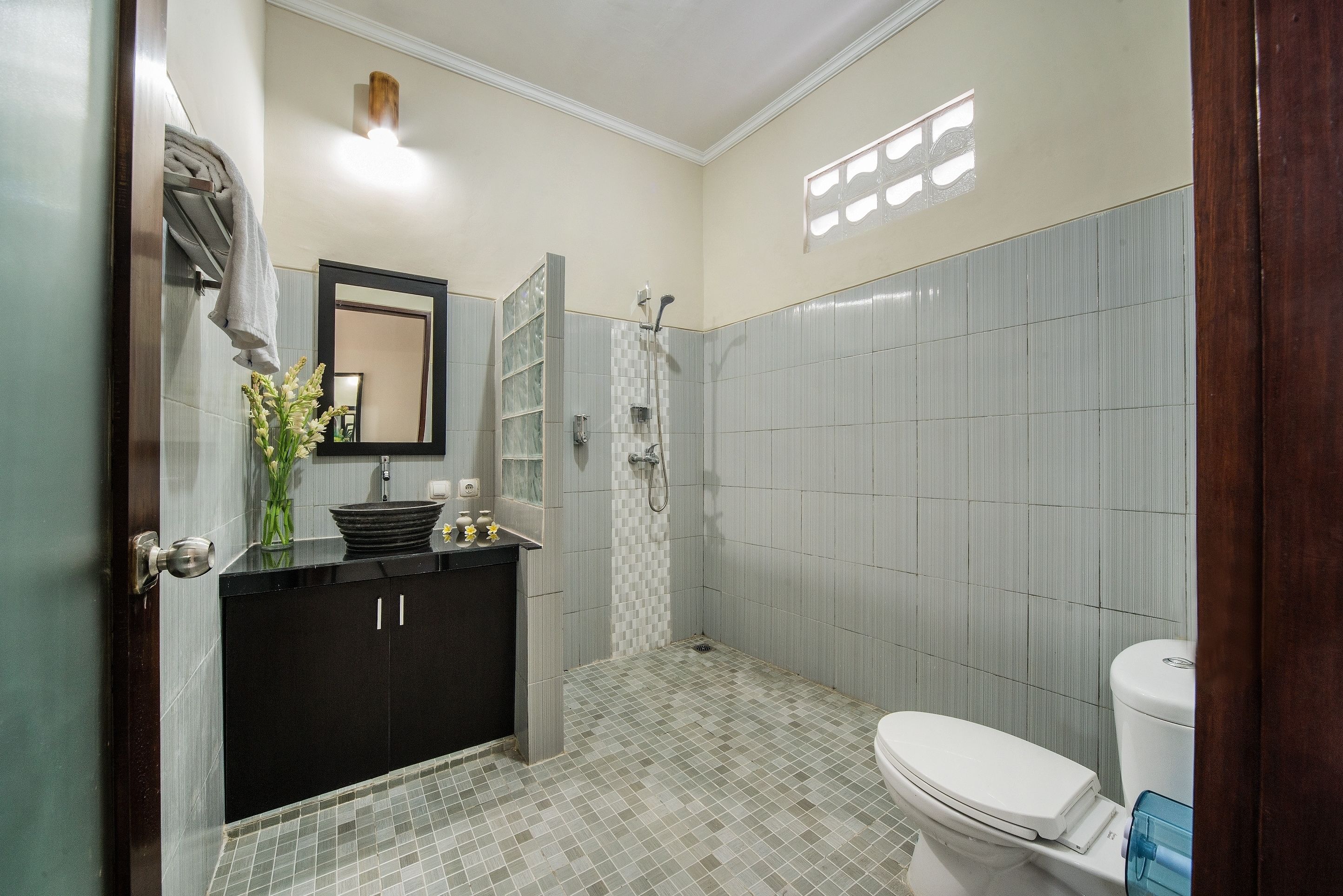 A bathroom with a black vanity, a white toilet, a shower, and a mirror above the sink.