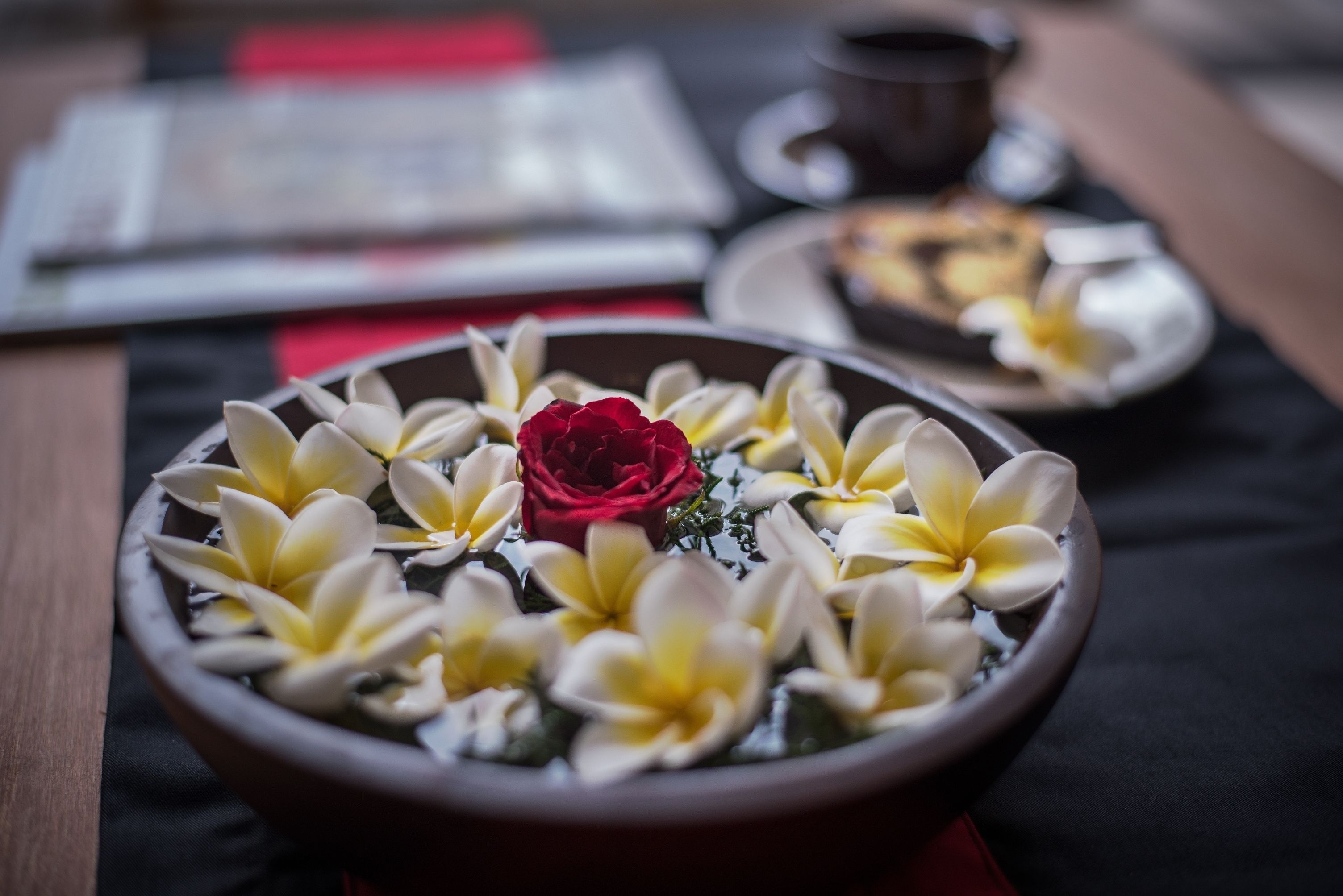 A bowl of flowers with a red rose and yellow and white blooms, placed on a table with a black tablecloth.
