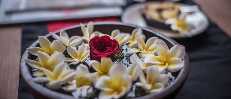 A bowl of flowers with a red rose and yellow and white blooms, placed on a table with a black tablecloth.