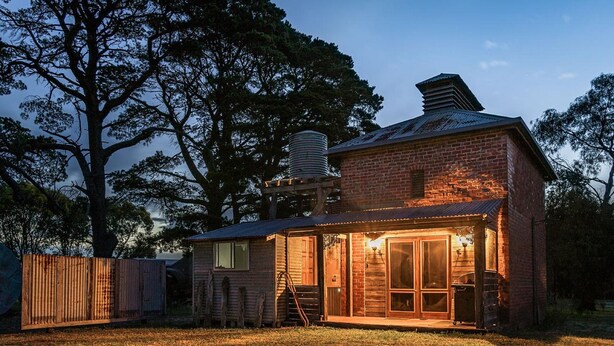 A rustic brick house with a metal roof, a wooden deck, and a large tree in the background. - GRAMPIANS HISTORIC TOBACCO KILN (Moutajup)