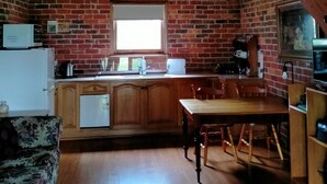 A rustic kitchen with brick walls, wooden beams, a dining table, and a sofa. - GRAMPIANS HISTORIC TOBACCO KILN (Moutajup)