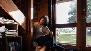 A person sitting by a window in a room with wooden floors, a bookshelf, and a staircase. - GRAMPIANS HISTORIC TOBACCO KILN (Moutajup)