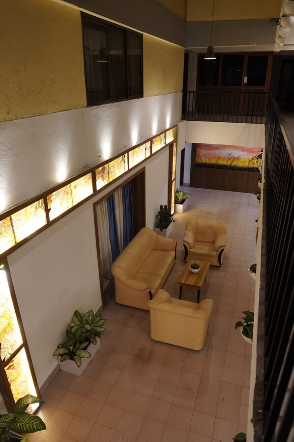 A spacious indoor area with a high ceiling, a balcony with a railing, and a seating area with sofas and a coffee table. - Hotel Luciya International (Mysore)