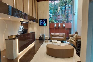 Un moderno vestíbulo de hotel con mostrador de recepción, un televisor de pantalla plana grande, un área de descanso cómoda y vistas al exterior.