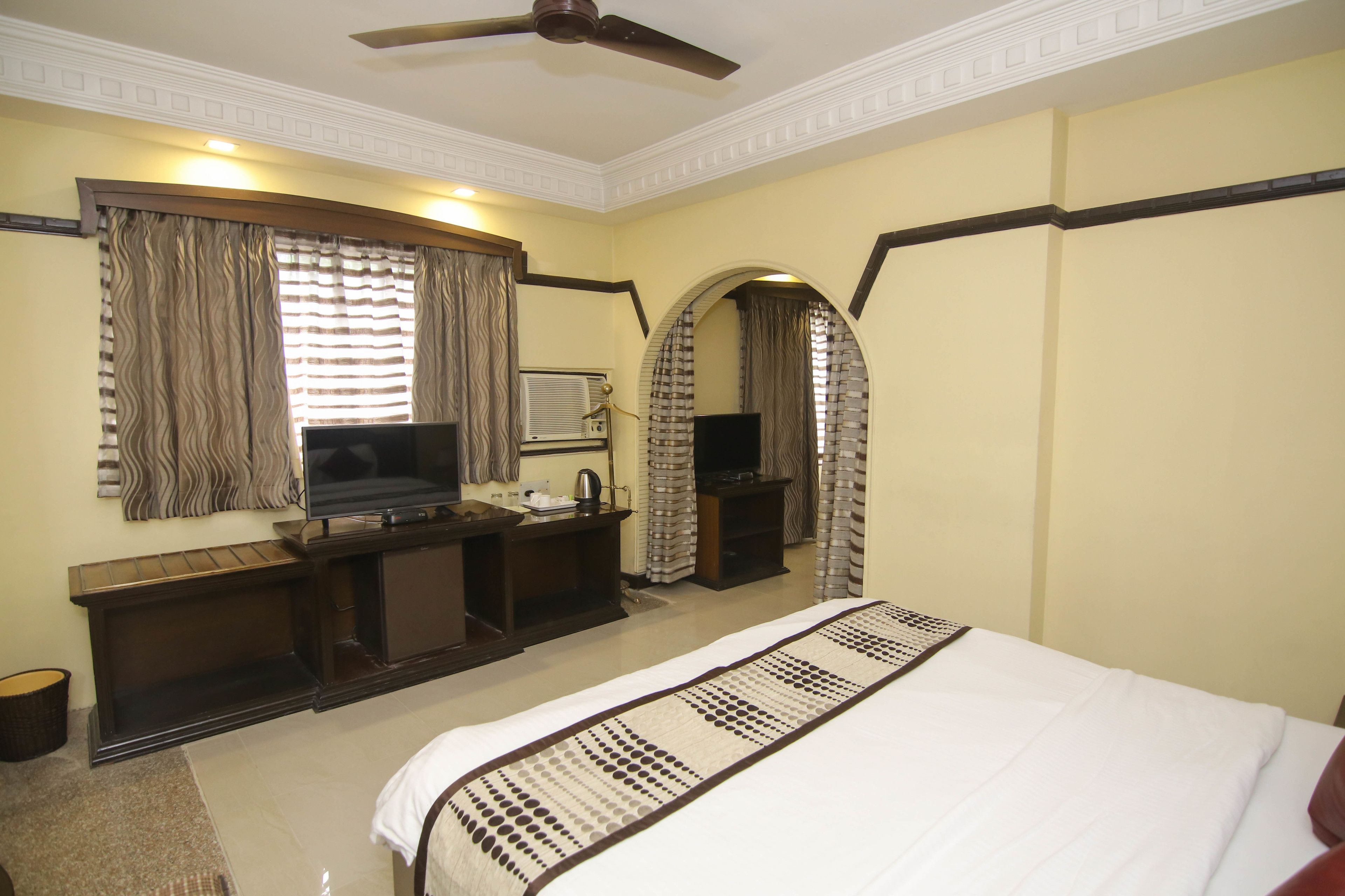 A hotel room with a bed, a desk with a television, a ceiling fan, and a large mirror.