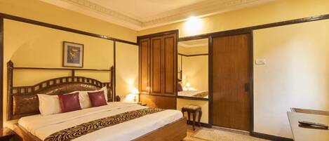 A hotel room with a large bed, wooden headboard, a mirror, a desk, and a wardrobe.