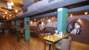 A restaurant with wooden floors, bar stools, and a mural on the wall. - Lytton Hotel (Kolkata)