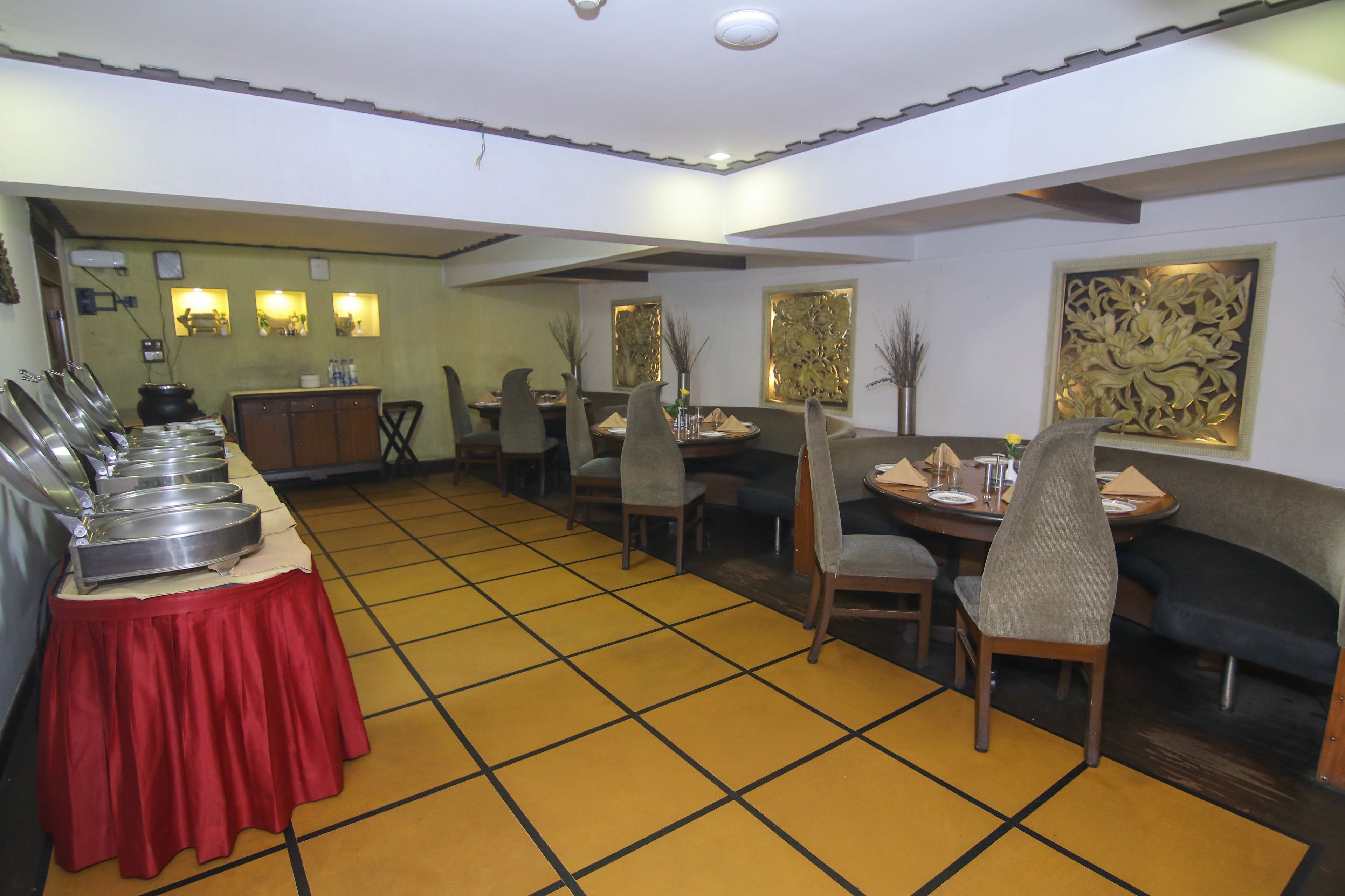 A dining area with multiple tables and chairs, a buffet line with food containers, and decorative wall art.