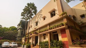 A building with a beige facade, multiple balconies with potted plants, and a parking area with two cars. - Lytton Hotel (Kolkata)