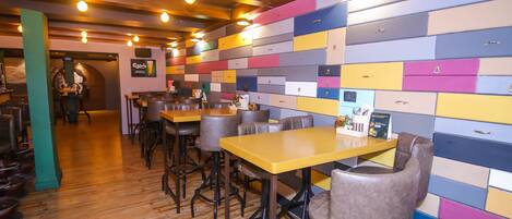 Un interior de restaurante con suelos de madera, varias mesas y sillas, y una pared colorida con cajones.