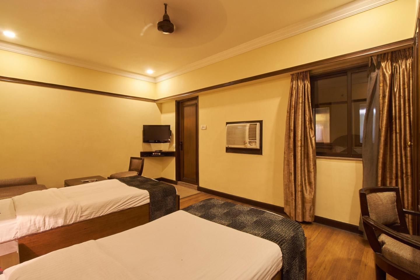 Quarto de hotel com duas camas, televisão, aparelho de ar condicionado e uma cadeira.