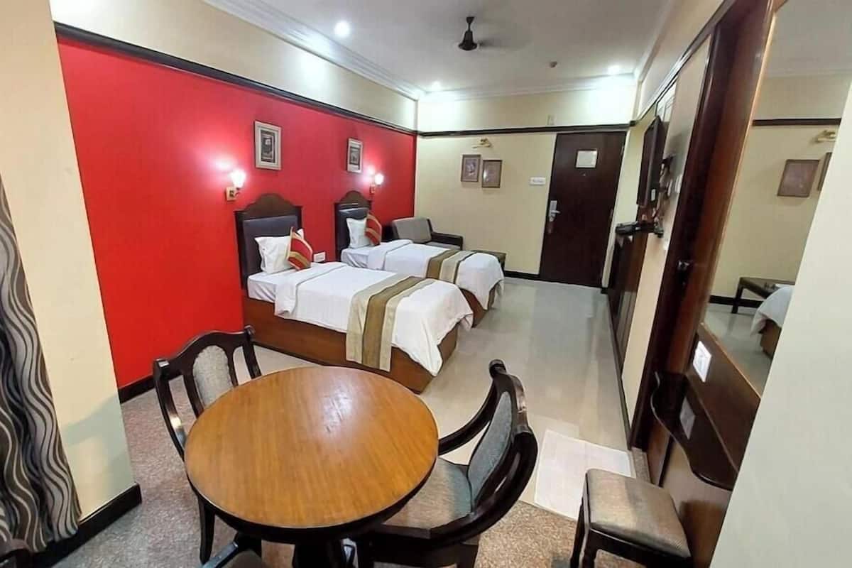 A hotel room with a red accent wall, two beds, a wooden table, and a chair.